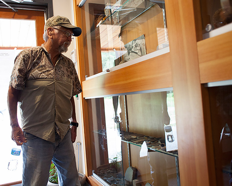A man wearing a baseball cap looks at artifacts in a glass case.