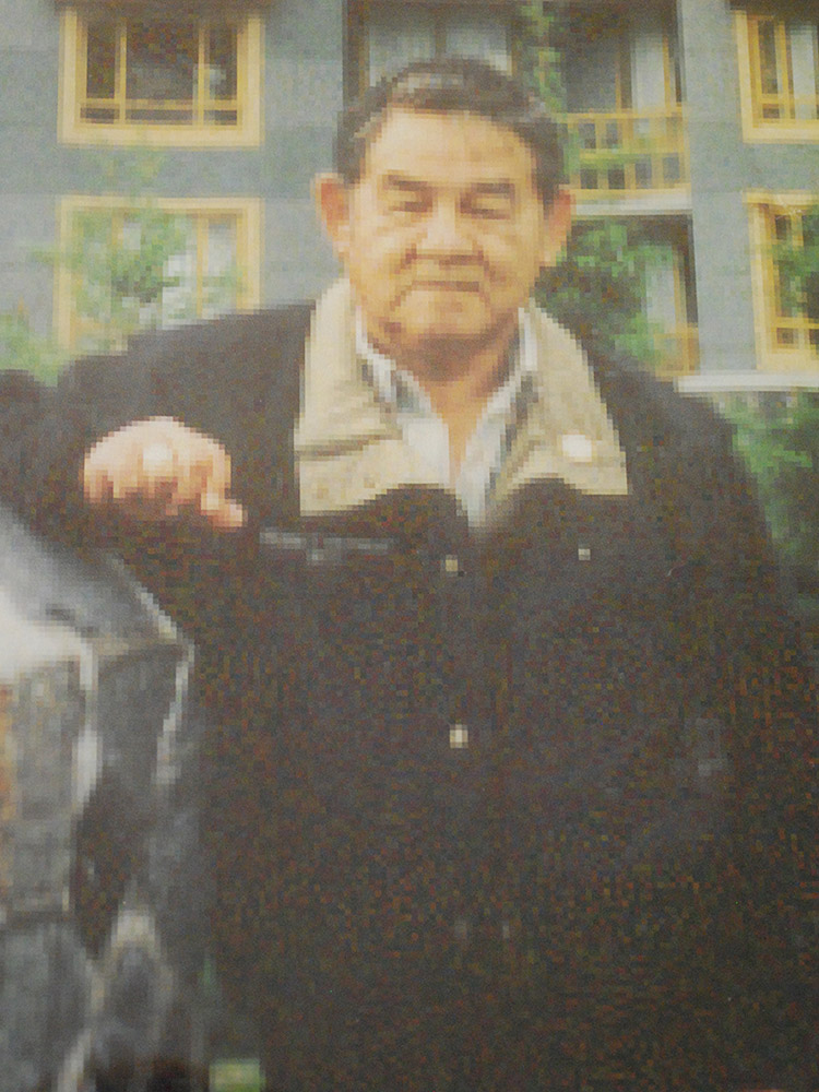 Un homme debout devant un immeuble bleu est accoté à un mur de pierres.