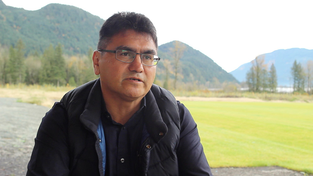 Un homme est assis devant un terrain de soccer et parle à une caméra vidéo.