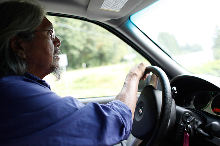 A man is driving a car. He is staring out the windshield and is wearing a blue shirt.