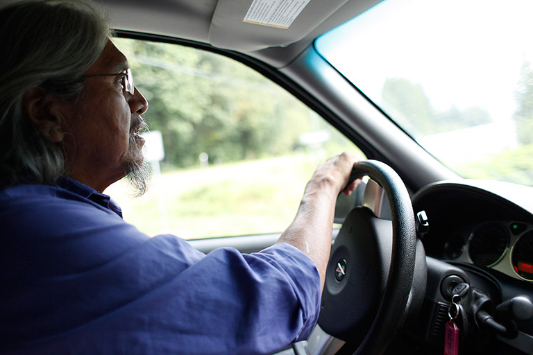 Un homme conduit une voiture. Il regarde devant lui et il porte une chemise bleue.