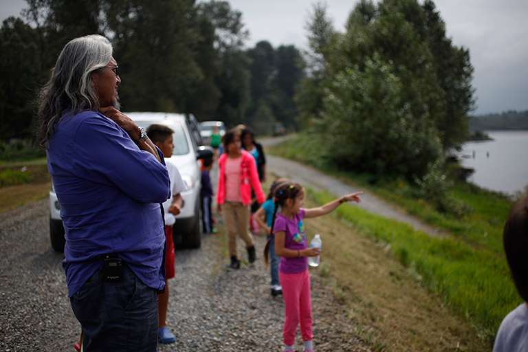 Au premier plan, un homme regarde vers le lac. Les enfants sont groupés près de la rive, regardent le lac et pointent vers le lac.