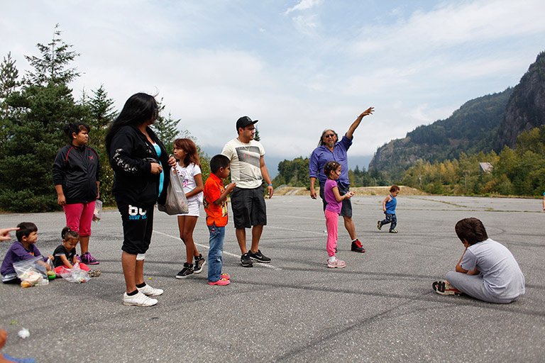 A group of children and adults are gathered outside, listening to their elder tell stories about the landscape.