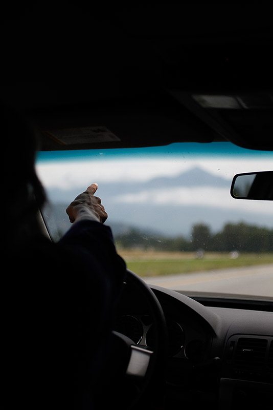 A person driving a car points at the mountain ahead in the distance.