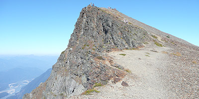 Au premier plan, il y a un champ et des arbres à feuilles caduques. Au loin, une montagne rocheuse.