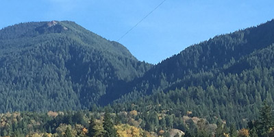 Une terre agricole avec des maisons en bordure et des montagnes boisées à l’arrière-plan.