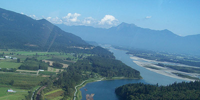 Farmland with houses in the mind-ground and forested mountains in the background.