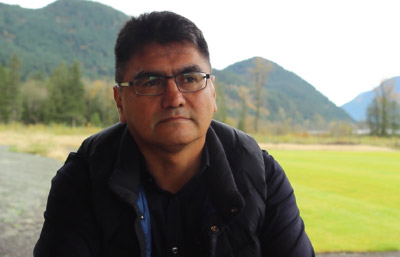 A man sits in front of a soccer field, talking to a video camera.