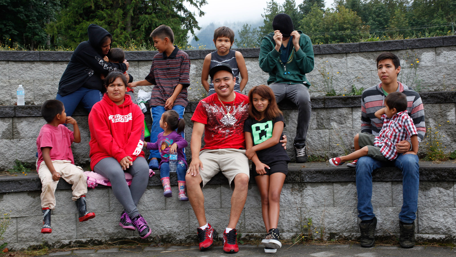 Children, youth  and adults, both male and female, are gathered around a picnic table serving food.