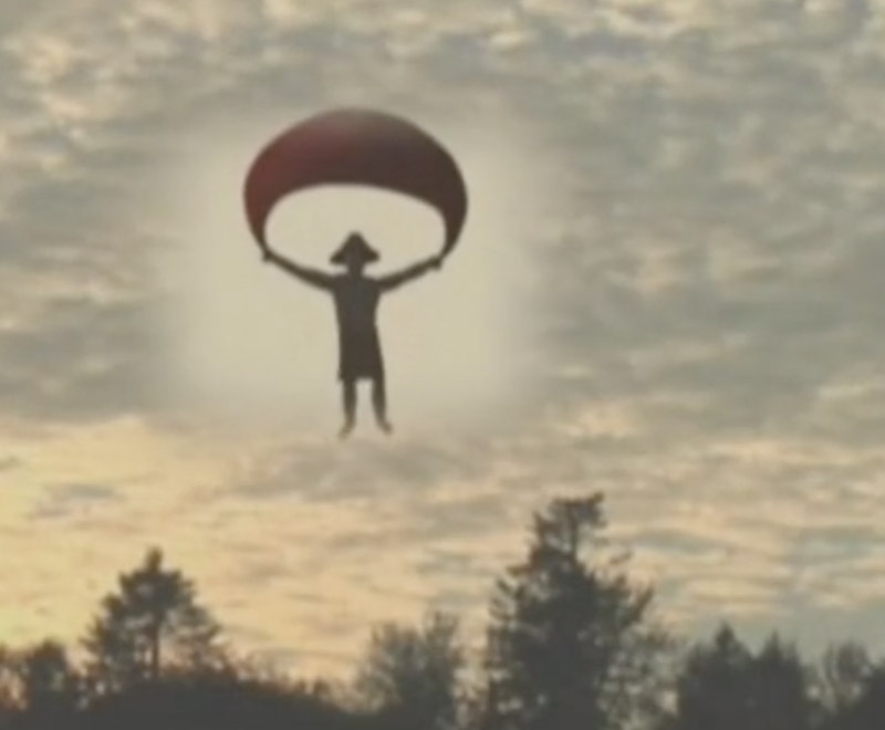 A figure with a cedar-root hat descends through the sky holding a parachute.