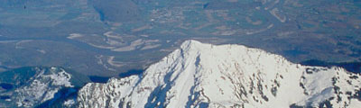 Vue aérienne d’une montagne au sommet enneigé et un paysage vert et montagneux à l’arrière-plan.